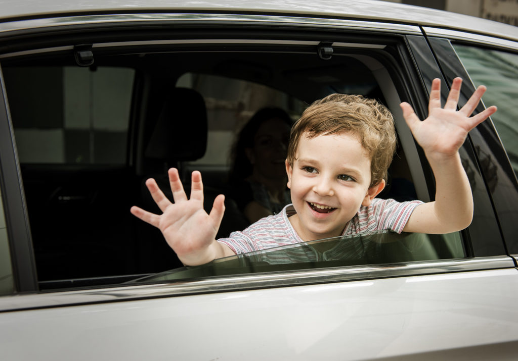 Boy waving to neighbours from car