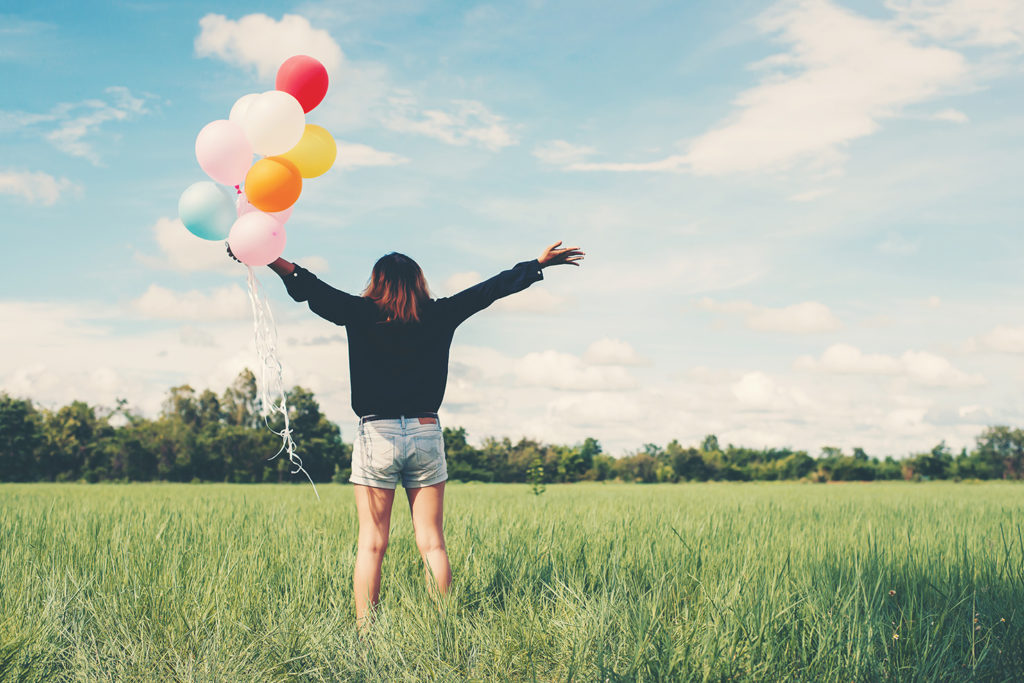 Girl on empty land in the sun with balloons